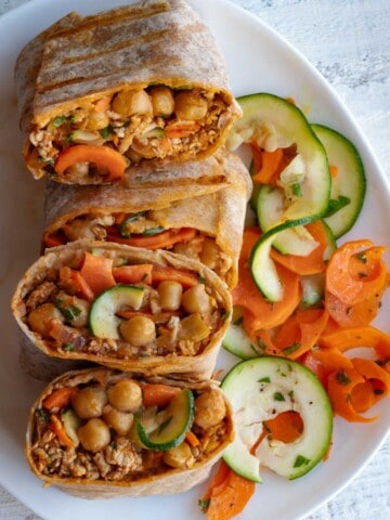 Two high-protein veggie wraps cut open on a white plate with a carrot and zucchini salad.