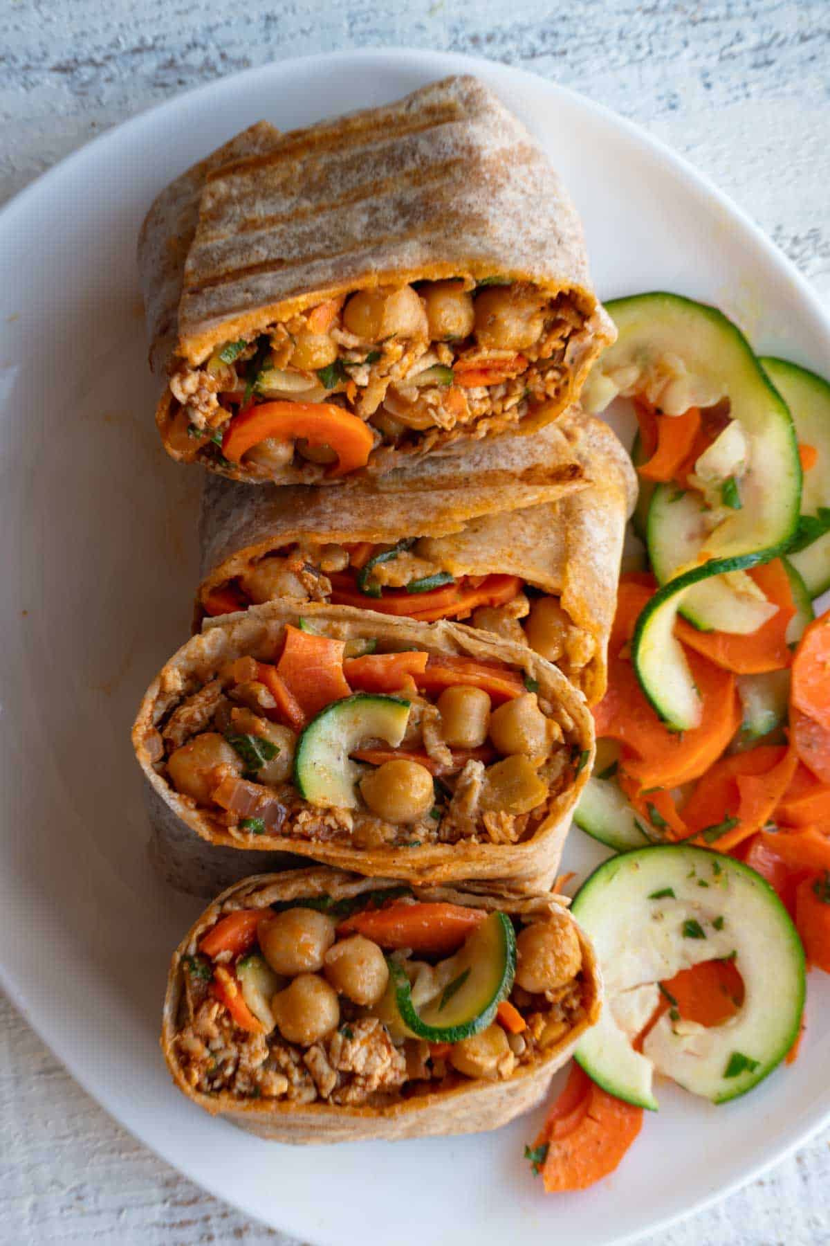 Two high-protein veggie wraps cut open on a white plate with a carrot and zucchini salad.