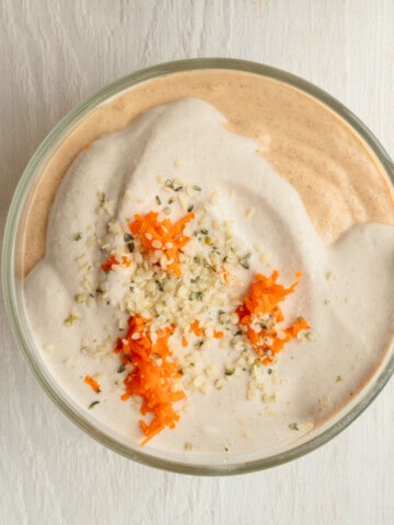 Blended chia pudding in a bowl topped with vegan nut cream, grated carrots, and hemp seeds.