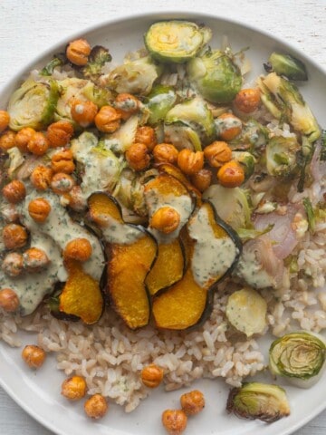 Vegan chickpea rice bowl with roasted Brussels sprouts, shallots, and acorn squash with green tahini dressing.