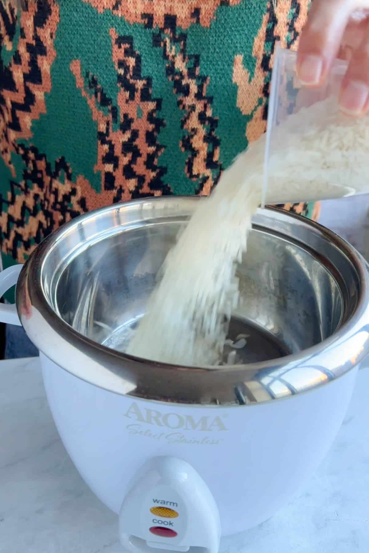 Pouring white rice into the bowl of an Aroma cooker.