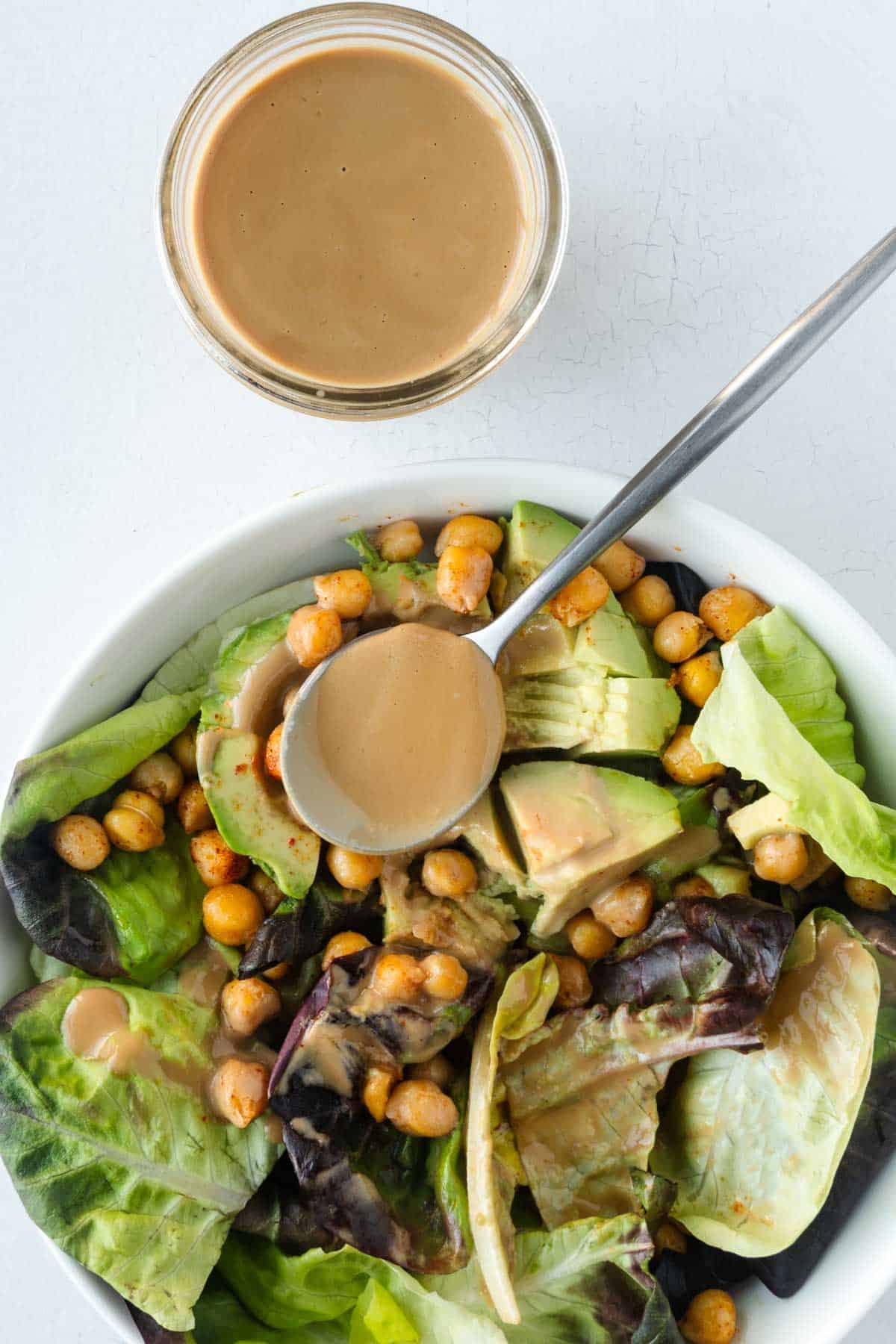 Healthy homemade balsamic vinaigrette dressing in a glass storage jar next to a bowl of salad.