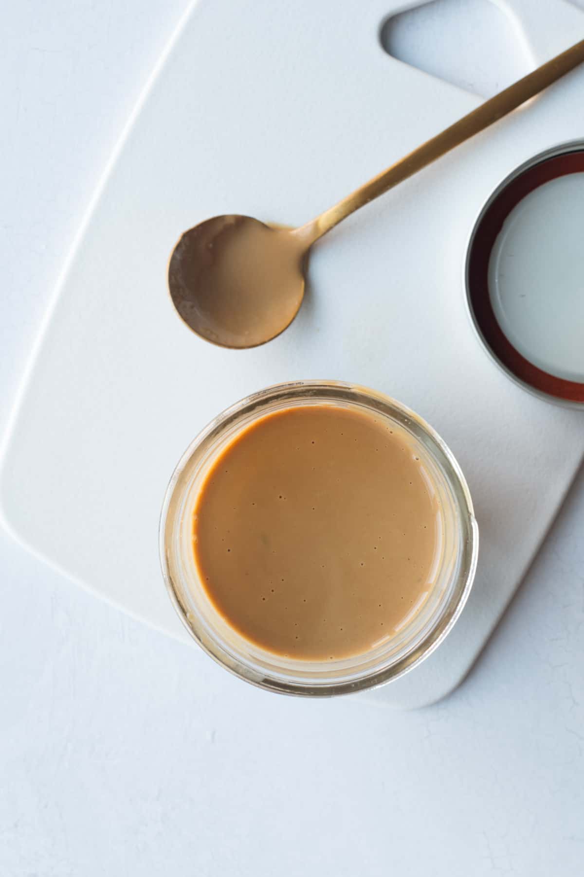 Healthy balsamic vinaigrette dressing in a glass storage jar next to a spoon with dressing.