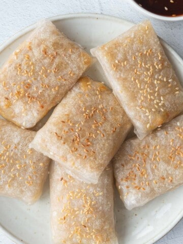 Vegan rice paper dumplings with sesame seeds on a white plate.