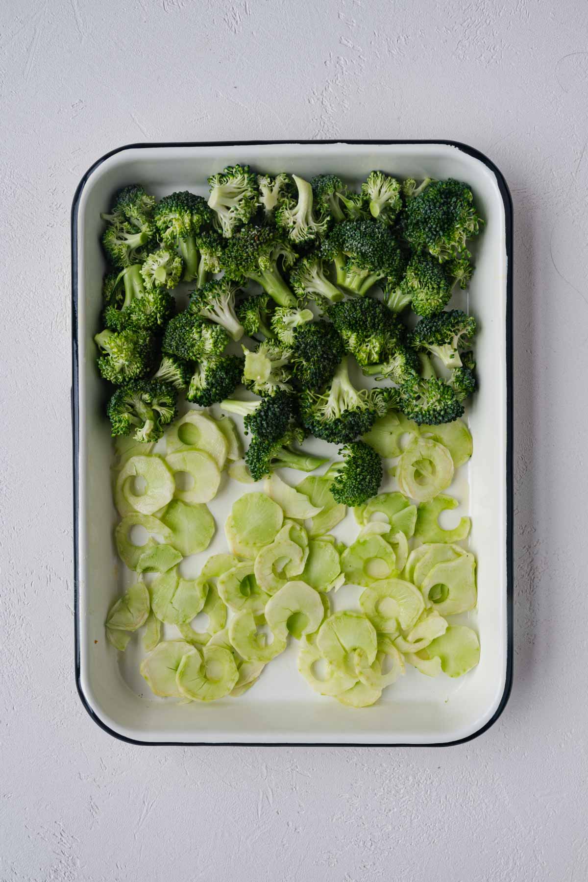 Broccoli florets and shaved stems on a white baking sheet.