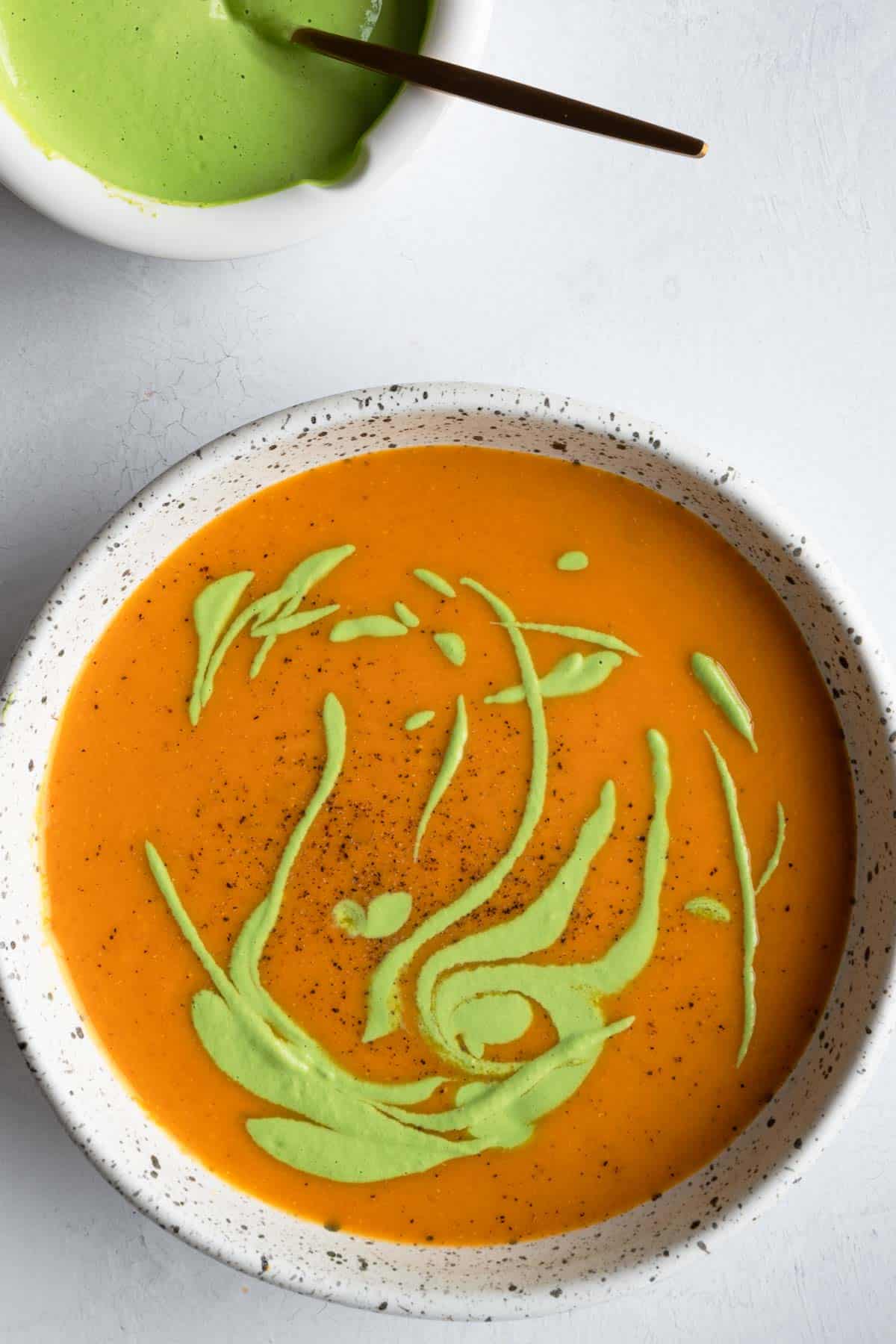 Butternut squash red lentil soup in a white bowl with a green sauce drizzled on top.