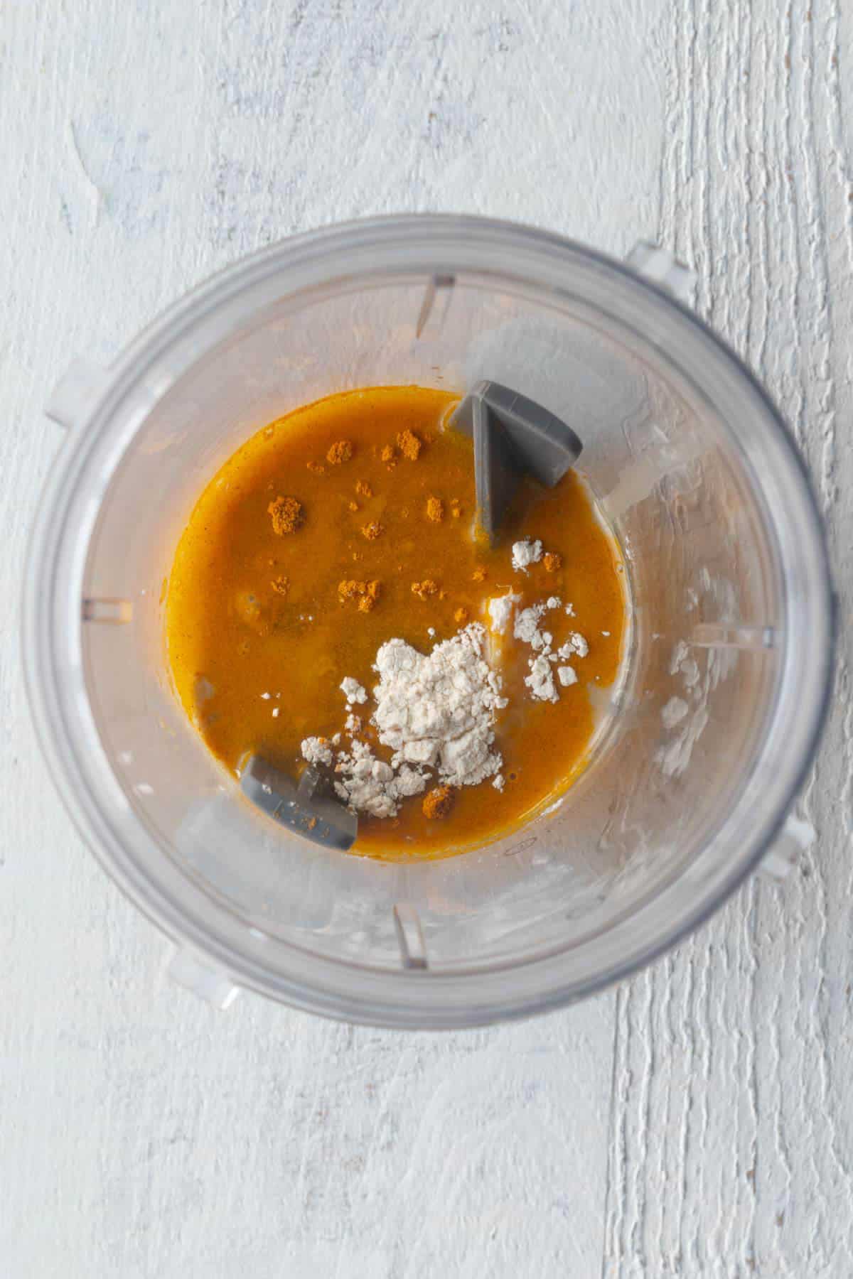 Turmeric, tahini, garlic powder, curry powder and ginger in the canister of a blender.