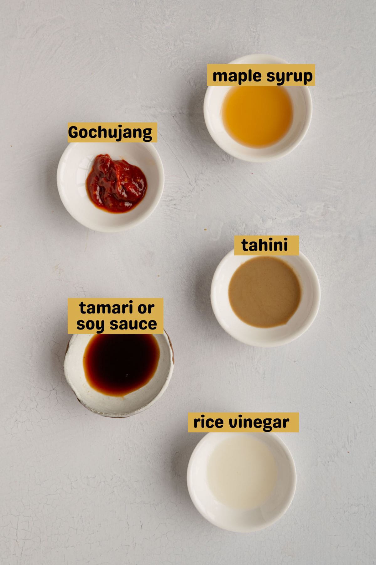 Maple syrup, gochujang, tahini, tamari, and rice vinegar in white bowls.