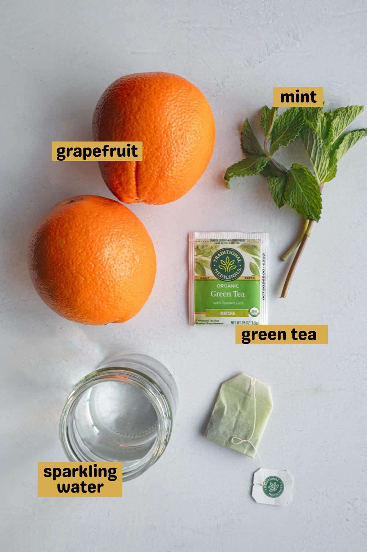 Two grapefruit, fresh mint, two green tea bags, and a jar of sparkling water.