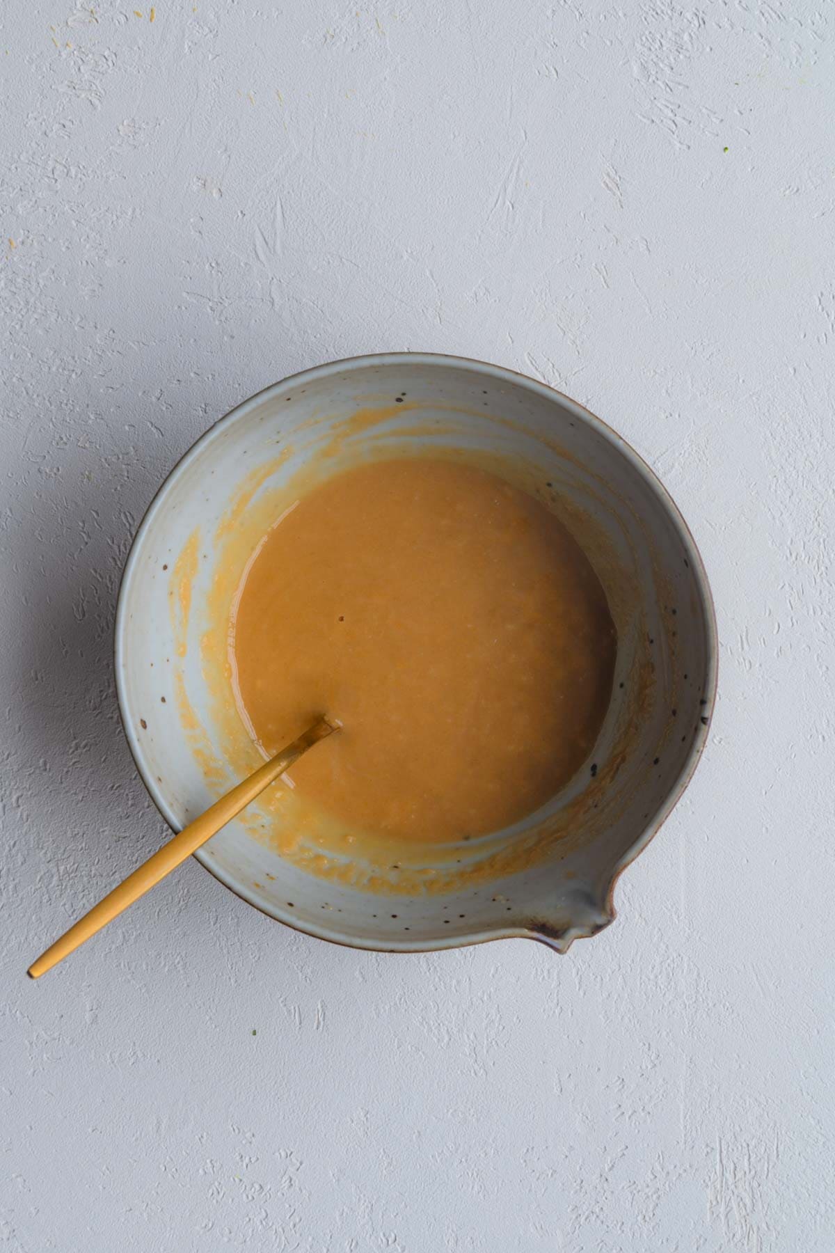 An orange colored dressing in a pourable bowl with a gold spoon.