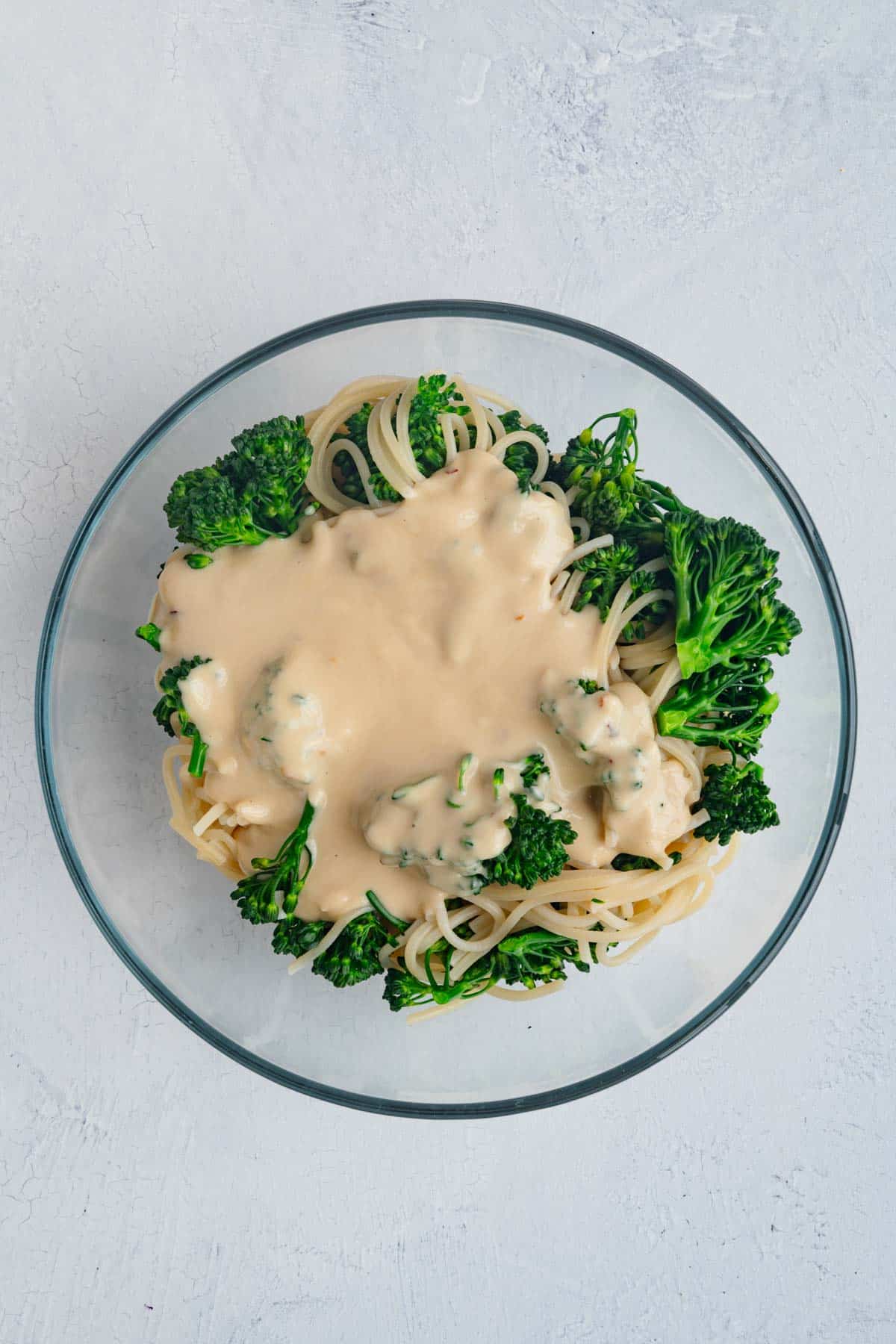 Pasta, noodles, and broccoli with tahini sauce in a glass bowl.