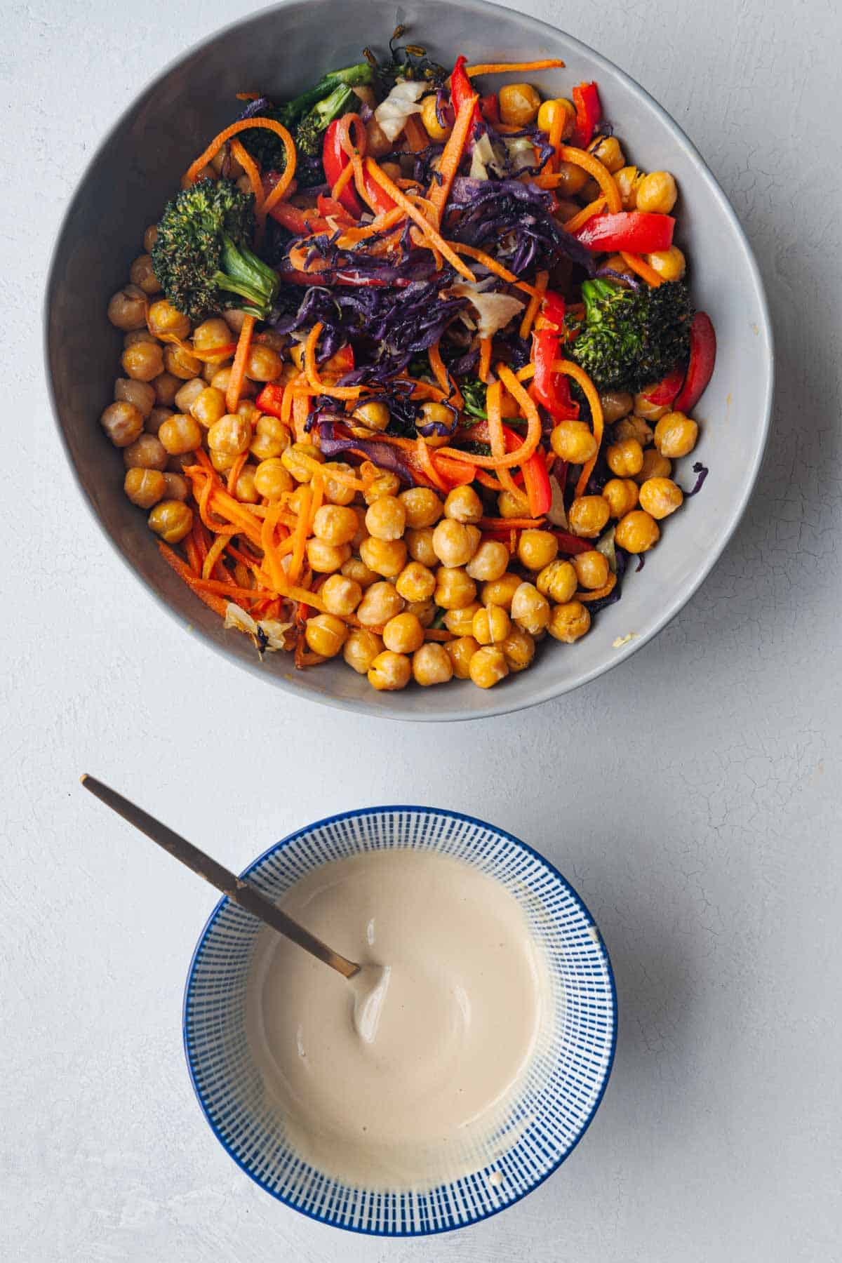 Roasted vegetable salad with chickpeas and broccoli next to a bowl with tahini dressing.