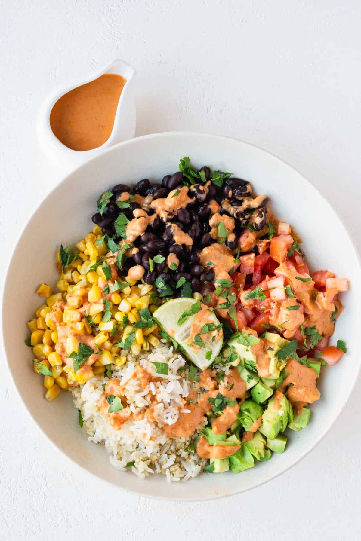 Baja bowl with rice, quinoa, avocado, tomatoes, black beans, corn, lime, and Bala sauce drizzled on top.