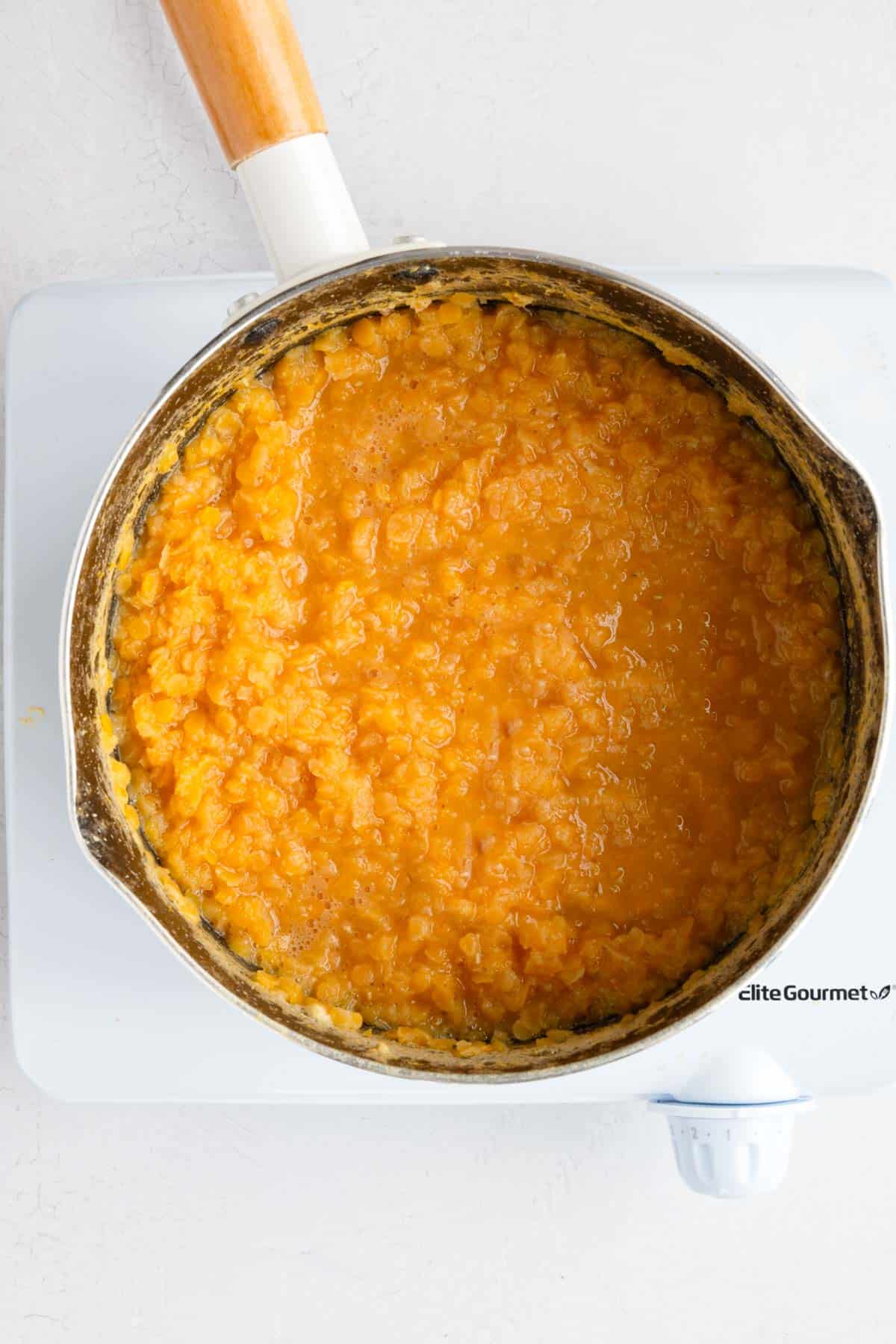 Red lentils cooking in a white saucepan.