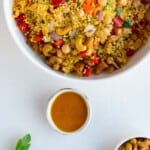 Golden dressing in a small white bowl next to a couscous salad and roasted cashews.