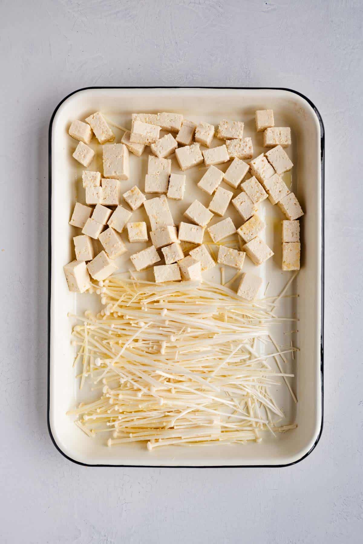 Enoki mushrooms and cubed firm tofu on a white baking sheet.