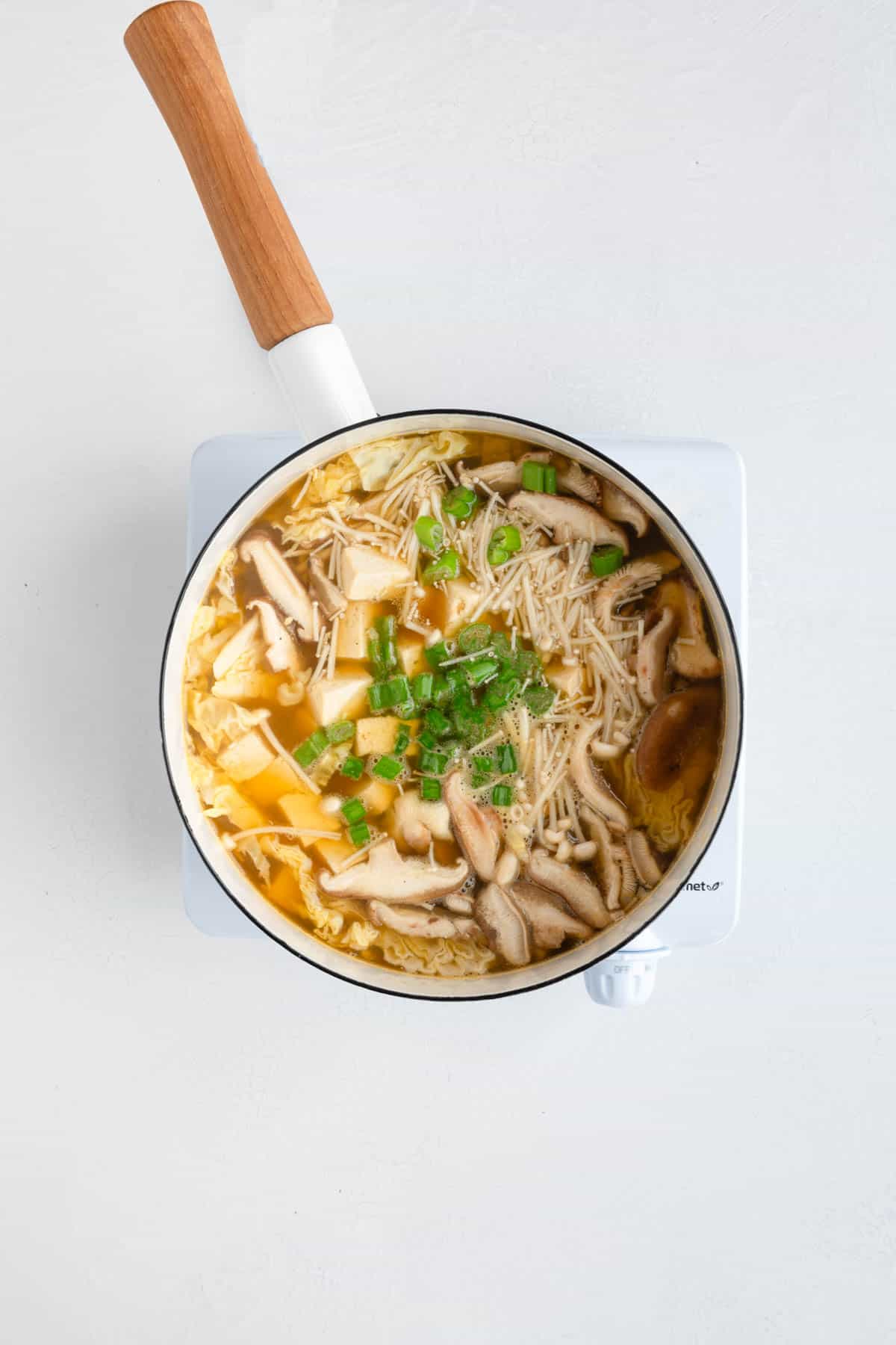 Miso soup with noodles, mushrooms, tofu, and green onion in a white saucepan.