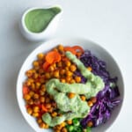 Avocado salad dressing on a bed of chopped red cabbage, carrot, green onion, and roasted chickpeas next to a white jar of avocado dressing.