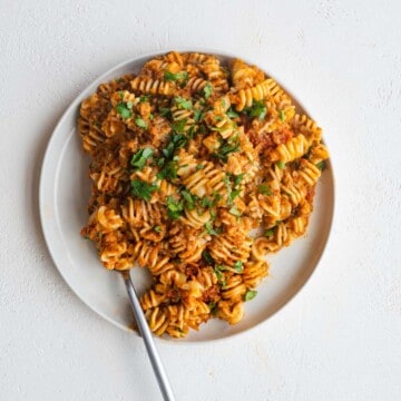 Vegan ragu with pasta and parsley on a white plate with a silver fork.