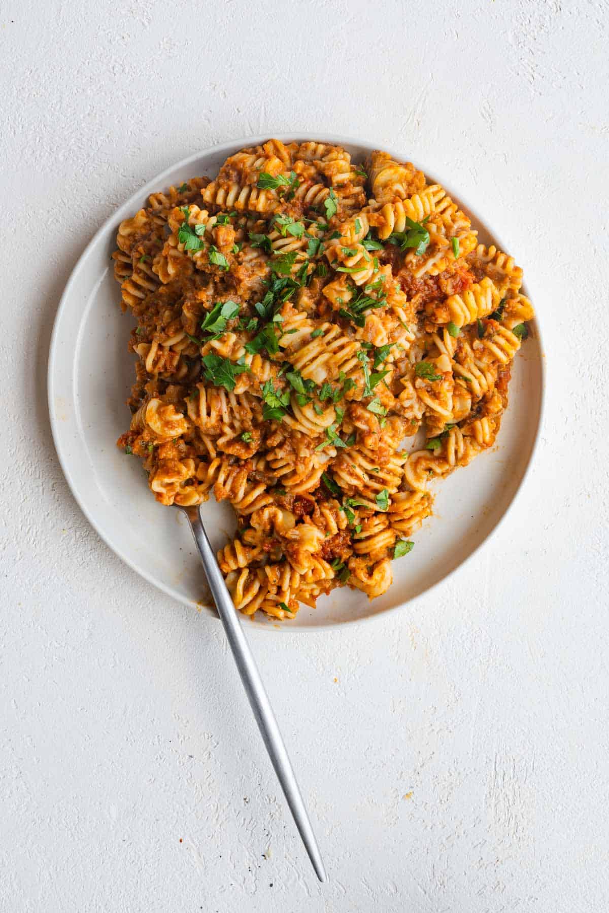 Vegan ragu with pasta and parsley on a white plate with a silver fork.