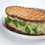 Mashed chickpeas in green sauce with arugula in a sandwich on a white plate.
