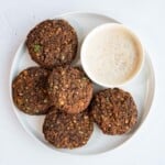 Five tempeh mushroom burgers on a white plate with a sauce.