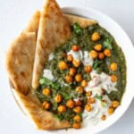 Chana saag with roasted chickpeas, pita, and Indian yogurt sauce in a white bowl.