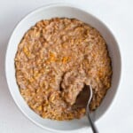 Creamy cooked oat groats in a bowl with a spoon.