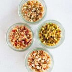 Four glass containers with chopped nuts, seeds, and dates.