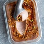Scooped chocolate no-churn ice cream in a glass container topped with pistachios and date syrup.