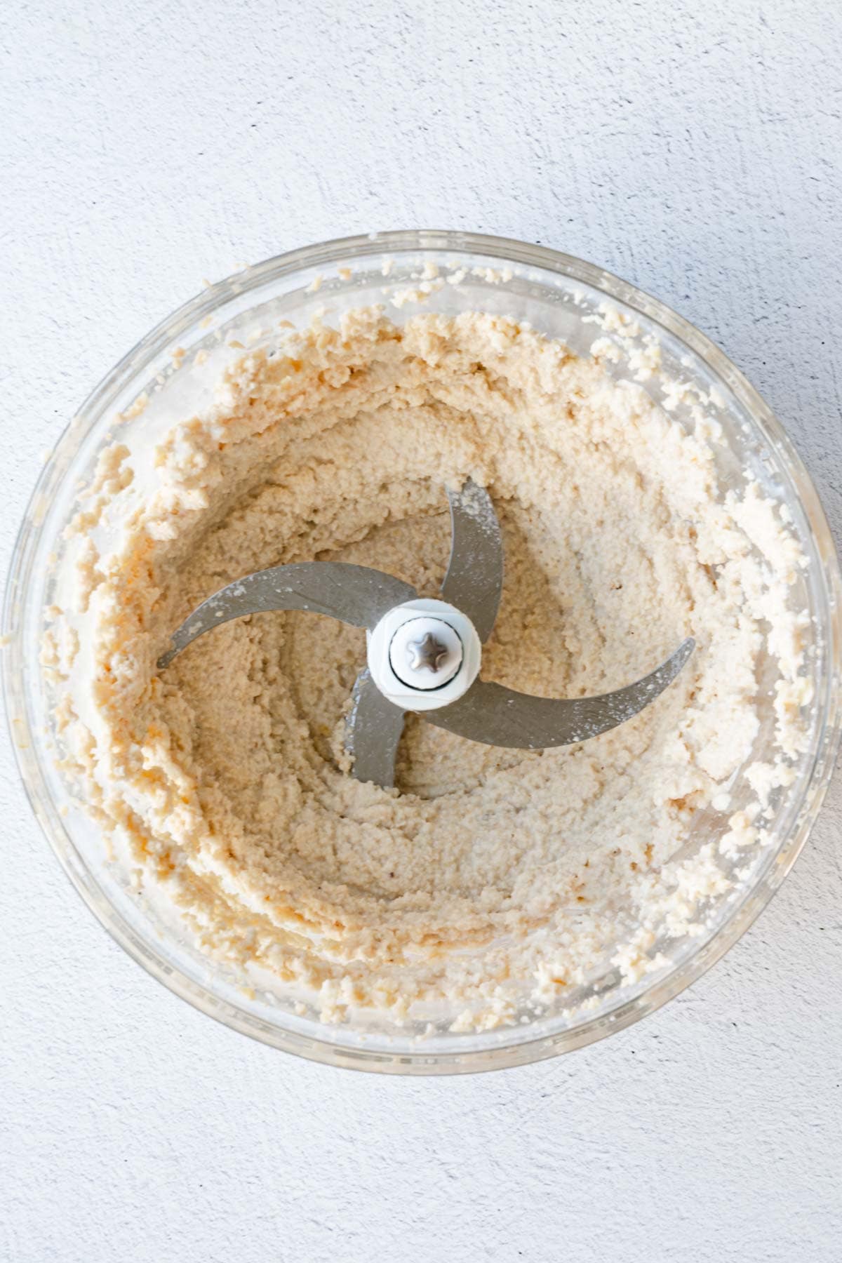 Blended chopped cashews in the canister of a food processor.