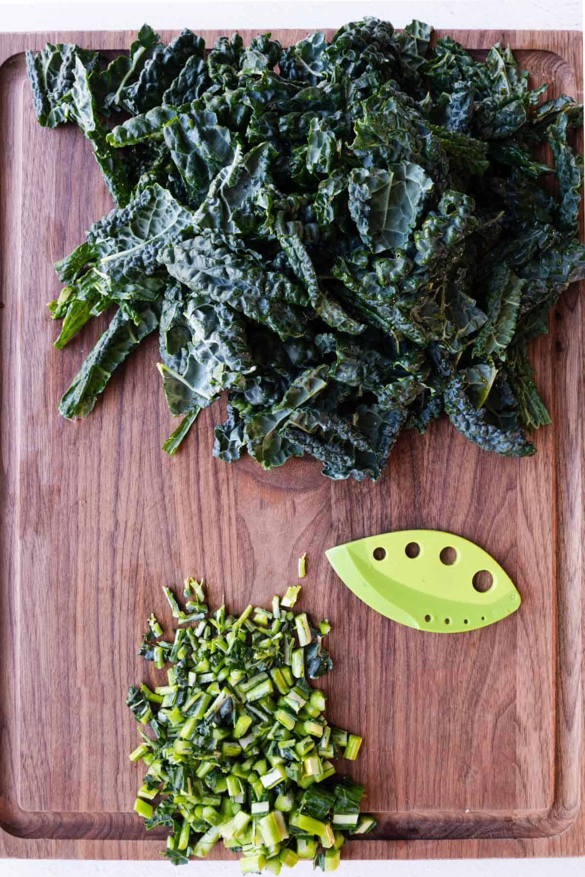 Chopped kale leaves and stems on a wooden cutting board with a stemming tool.