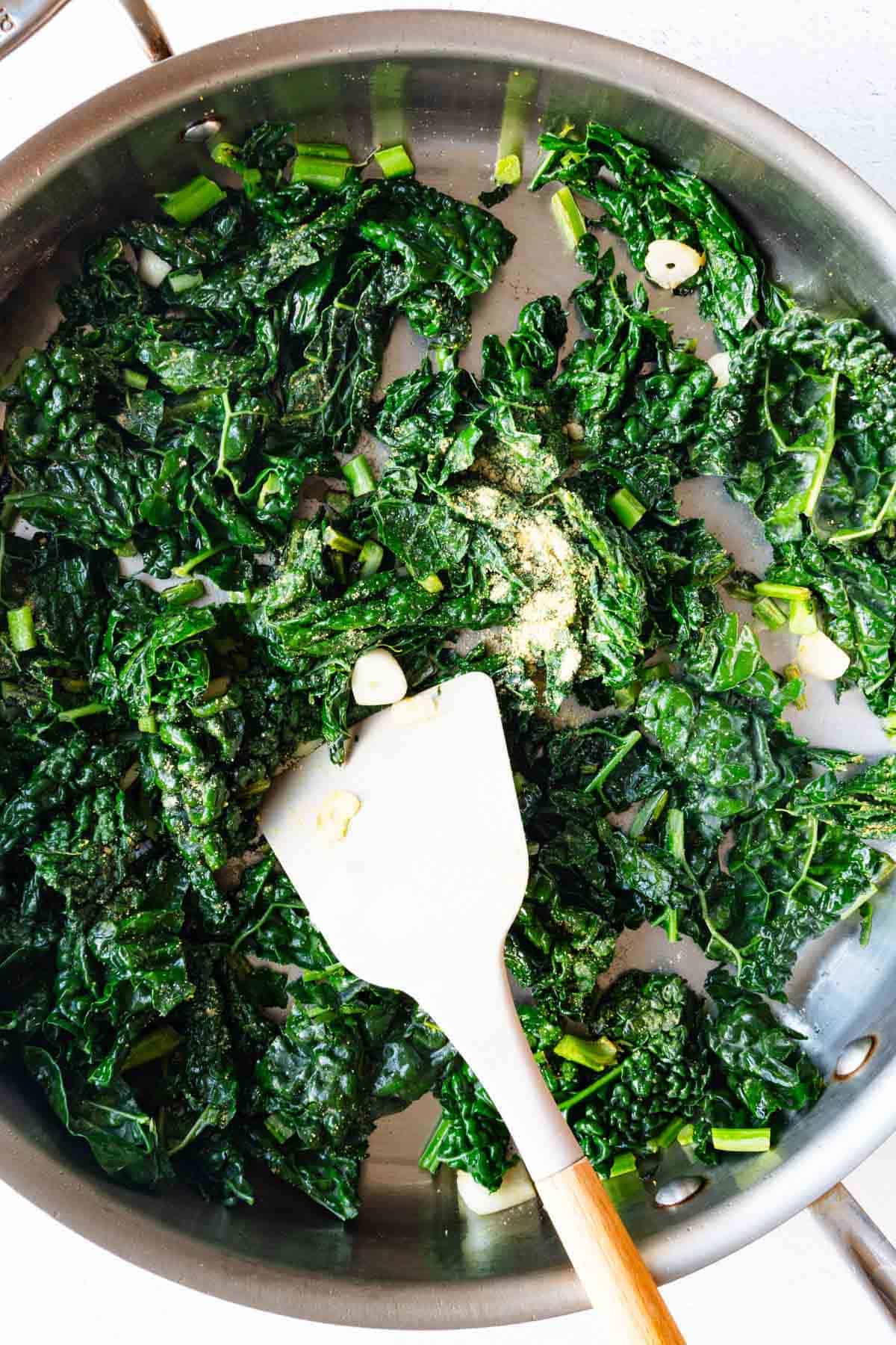 Cooked kale with garlic and mustard powder in a stainless steel skillet.