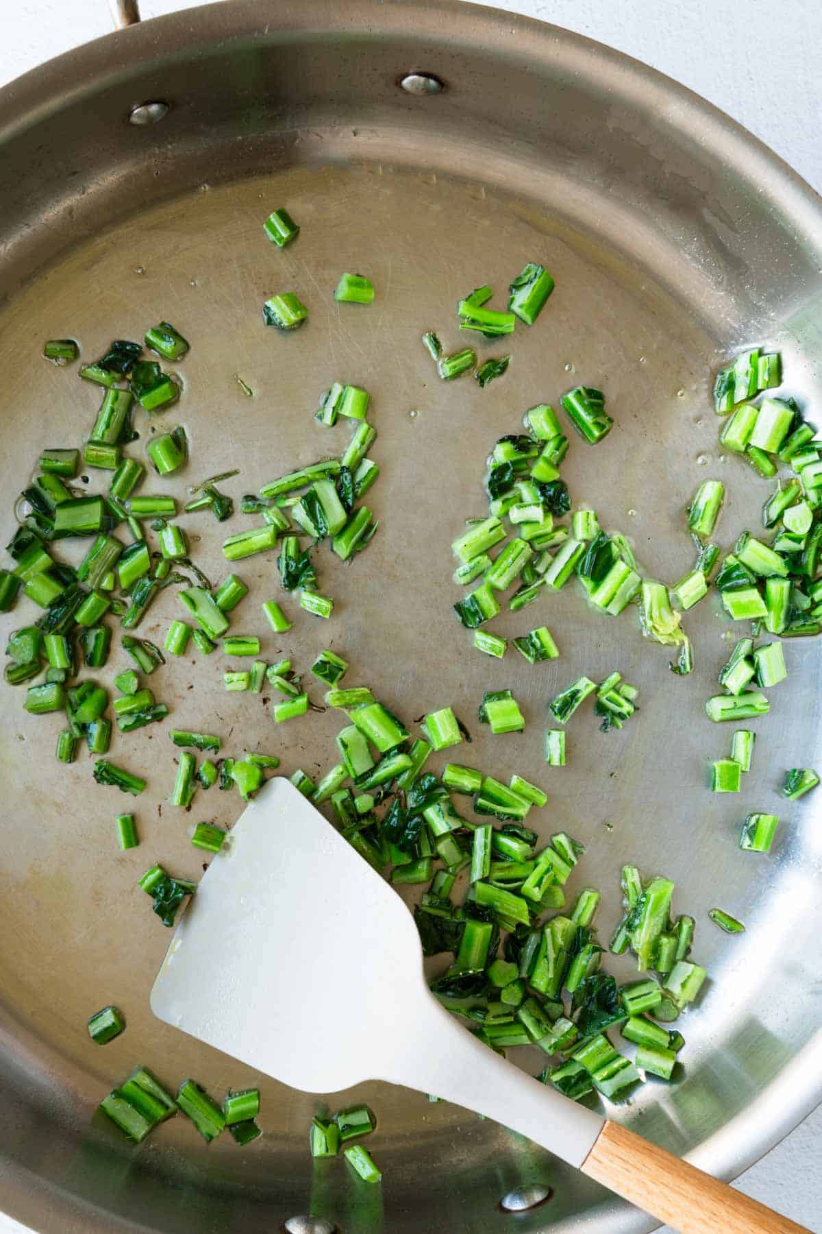 Chopped kale stems cooking in a stainless steel skillet.