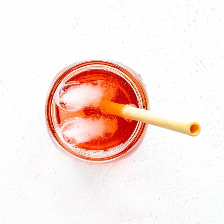 Cranberry water with ice in a mason glass with a bamboo straw.