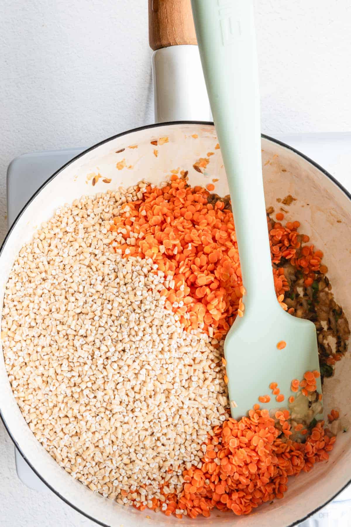 Red lentils, steel cut oats, and cooked onion, garlic, and chili pepper in a white saucepan.