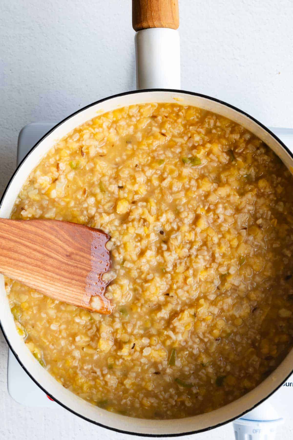Cooked savory oats in a white saucepan with a wooden spatula.