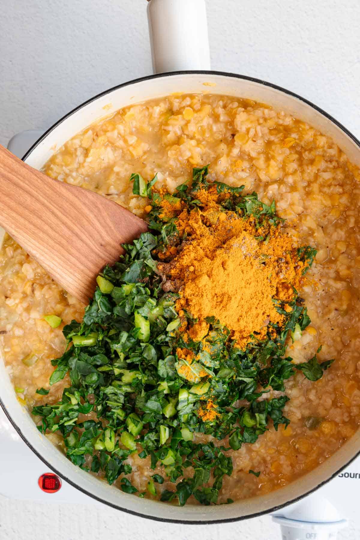 Red lentils, steel-cut oats, kale, and spices cooking in a white skillet.