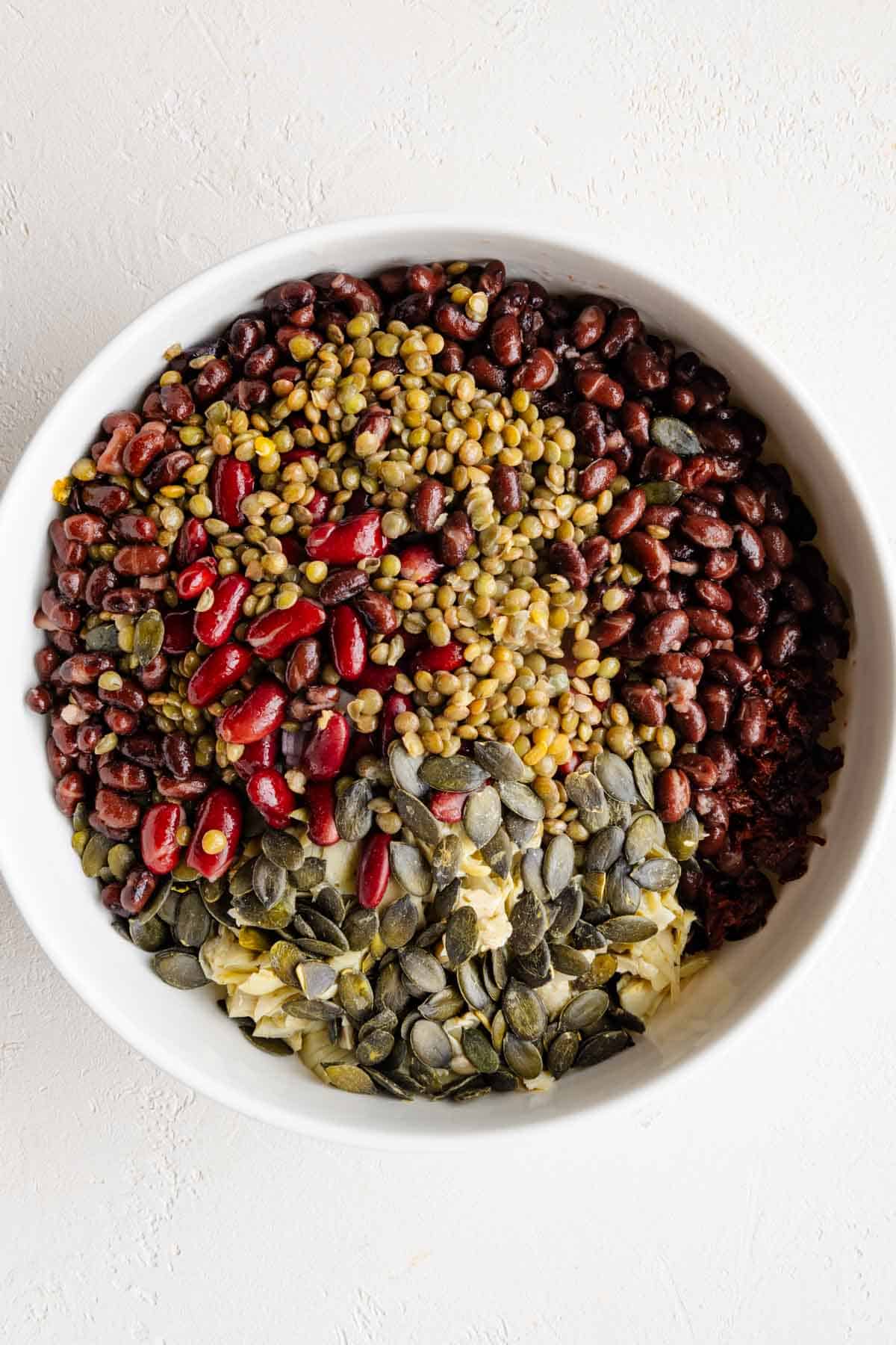 Dense bean salad with kidney beans, black beans, lentils, and artichoke hearts in a white bowl.