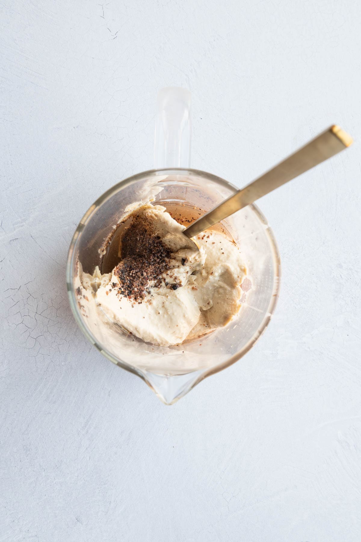 Mixing hummus, lemon, red wine vinegar, and seasoning in a glass pyrex with a whisk.