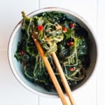 Wakame seaweed, glass noodles, red chili pepper, garlic, and dressing in a small bowl with chopsticks.