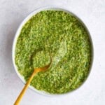 Pesto recipe without nuts in a white bowl with a gold spoon.