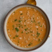 Vegan barley soup with white beans and vegetables in a bowl with a spoon.