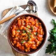 Sun-dried tomato beans in a bowl topped with cilantro on a wooden cutting board with a ladle.