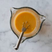 Miso dressing in a glass beaker with a metal whisk.