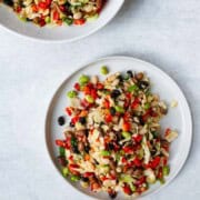 Mixed bean salad on a white plate and serving platter with cabbage and red bell peppers, edamame, black beans, white beans, and pinto beans.