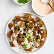 Seitan chicken pieces on a white plate with yogurt sauce and fresh herbs.
