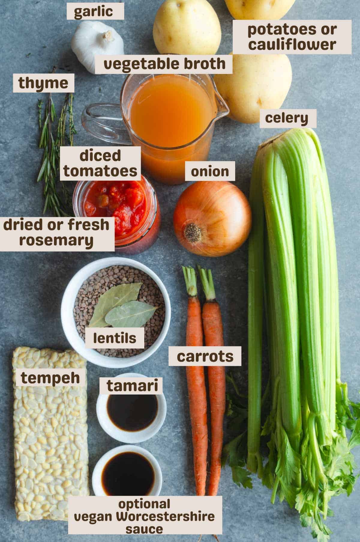 Yukon gold potatoes, celery, carrots, tempeh, brown sauce, lentils, bay leaves, onion, diced tomatoes, rosemary, thyme, garlic, and broth on a blue backdrop.