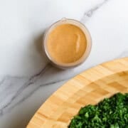 Low calorie salad dressing next to a wooden bowl of kale salad.