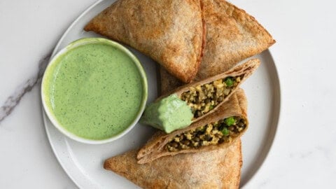 Samosa wraps made form tortillas with a high-protein filling on a white plate, with a green herb yogurt sauce.